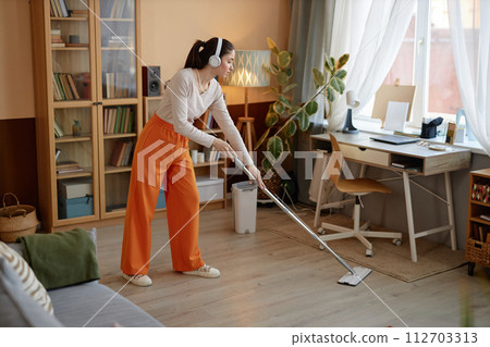 Full length portrait of young woman mopping floors and listening to music at home while enjoying cleaning copy space 112703313