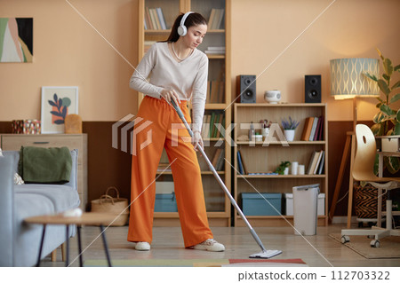 Full length portrait of young woman wearing headphones and mopping floors at home while enjoying cleaning copy space 112703322