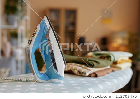 Close up background image of light blue iron on ironing board with stack of clothes copy space 112703459