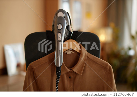 Close up of garment steamer appliance with clothes hanging on vertical ironing board copy space Close up of garment steamer appliance with clothes hanging on vertical ironing board copy space 112703467