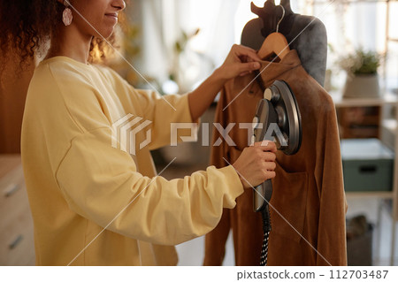 Side view closeup of smiling young woman using garment steamer on delicate velvet jacket copy space Side view closeup of smiling young woman using garment steamer on delicate velvet jacket copy space 112703487