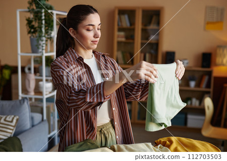 Waist up portrait of smiling young woman folding clothes on laundry day at home and enjoying chores copy space Waist up portrait of smiling young woman folding clothes on laundry day at home and enjoying chores copy space 112703503