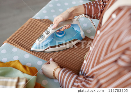 Top view closeup of young woman ironing clothes on ironing board on laundry day copy space Top view closeup of young woman ironing clothes on ironing board on laundry day copy space 112703505