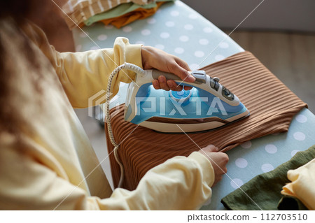 High angle closeup of unrecognizable woman ironing clothes with cute light blue iron appliance at home copy space 112703510