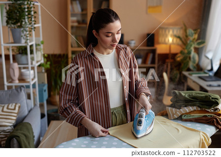 High angle portrait of young woman ironing clothes on laundry day and taking care of house chores copy space 112703522
