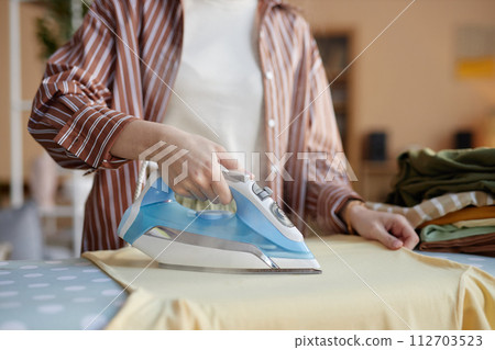 Closeup of unrecognizable woman ironing clothes with steaming blue iron at home copy space 112703523