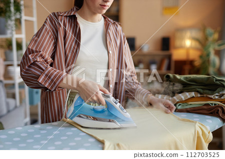 Close up woman ironing clothes on ironing board and taking care of house chores on laundry day copy space Close up woman ironing clothes on ironing board and taking care of house chores on laundry day copy space 112703525