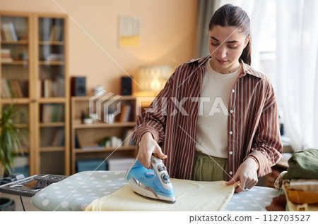 Waist up portrait of Caucasian young woman ironing clothes on ironing board while taking care of house chores on weekend copy space 112703527