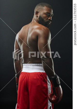 Vertical back view of muscular African American boxer posing shirtless and wearing boxing gloves 112703533