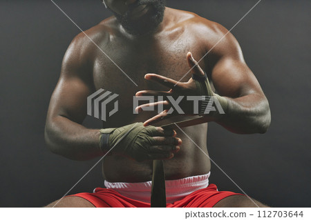 Dramatic cropped shot of fighter wrapping hands in bandages against smokey black background 112703644