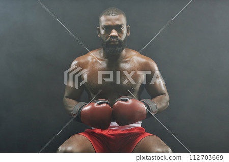 Front view portrait of tough African American boxer wearing red gloves and looking at camera sitting against black background Front view portrait of tough African American boxer wearing red gloves and looking at camera sitting against black background 112703669