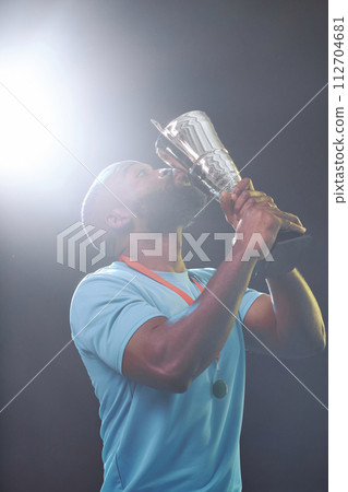 Vertical portrait of sportsman kissing trophy cup and celebrating victory with lens flare 112704681