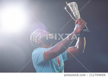 Side view portrait of African American sportsman holding trophy cup and cheering while celebrating victory with lens flare copy space Side view portrait of African American sportsman holding trophy cup and cheering while celebrating victory with lens flare copy space 112704689