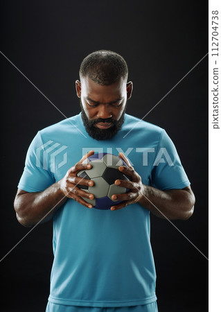 Vertical portrait of muscular African American man as football player holding ball to chest and looking down Vertical portrait of muscular African American man as football player holding ball to chest and looking down 112704738