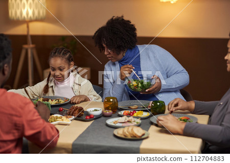 Portrait of mother talking to young girl using smartphone at dinner table and watching videos online 112704883