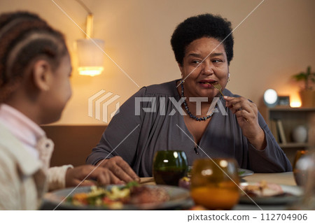 Portrait of African American senior woman enjoying dinner with family sitting at table together and eating food copy space 112704906