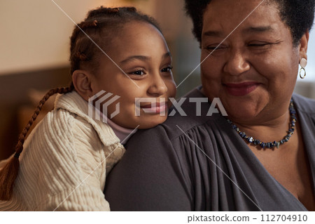 Close up portrait of cute African American little girl embracing smiling grandmother at home Close up portrait of cute African American little girl embracing smiling grandmother at home 112704910