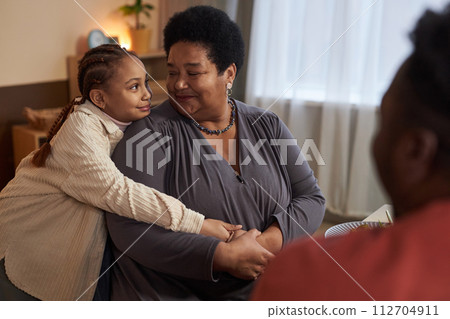 Side view portrait of cute Black little girl embracing grandmother during dinner with family at home 112704911