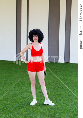 An athletic woman posing on a green lawn near a building An athletic woman posing on a green lawn near a building 112705352