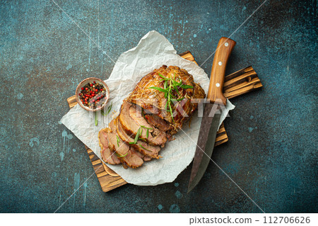 Rolled turkey roasted with spices and herbs on baking paper with knife and rustic concrete background top view. Baked cut for slices turkey fillet roll for dinner 112706626