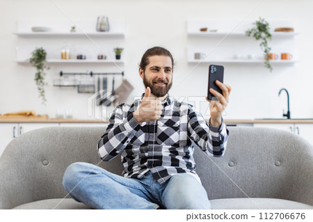 Caucasian male holding smartphone while have video call, sitting at couch. 112706676