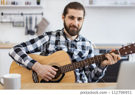 Smiling Caucasian man learning to play instrument using online lessons on laptop 112706951