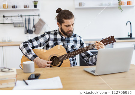 Bearded adult posing with guitar while enjoying pleasant pastime at home. 112706955