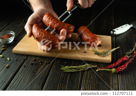 Preparing to grill sausages. Stringing Munich sausages on a fork by the hands of a cook on the kitchen table. Space for recipe or menu 112707111