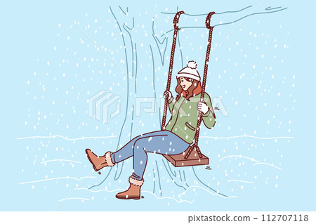 Woman swings on swing in winter park, rejoicing at falling snow and approach christmas or new year 112707118