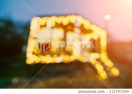 Abstract defocused bright Christmas lights on wooden house, creating decorative illumination in evening scene Abstract defocused bright Christmas lights on wooden house, creating decorative illumination in evening scene 112707204