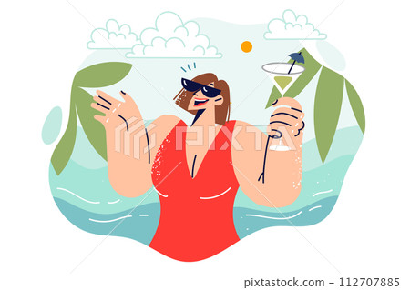 Woman drinks cocktail while standing on beach of tropical island with seashore and palm trees 112707885