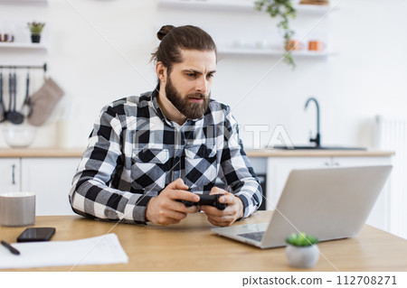 Caucasian guy in checkered shirt using remote console for playing video games. 112708271