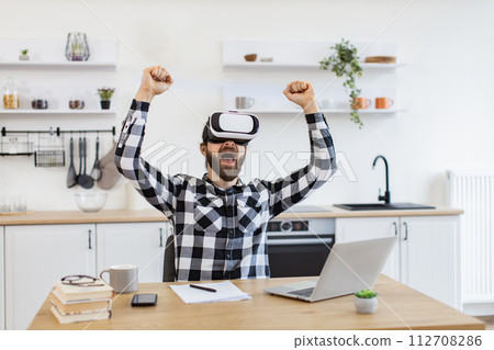 Bearded man wearing VR headset and gesturing from happiness. Bearded man wearing VR headset and gesturing from happiness. 112708286