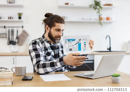 Caucasian male holding paper with charts while speaking during online meeting. 112708313
