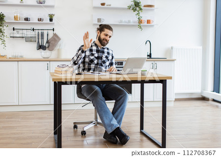 Bearded adult waving hello at webcam of computer while greeting colleague. 112708367