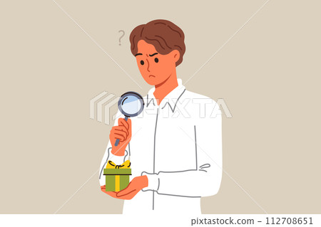 Business man examines suspiciously small gift box, using magnifying glass to spot catch Business man examines suspiciously small gift box, using magnifying glass to spot catch 112708651