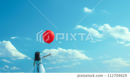 A girl holding a balloon and looking up at the blue sky 112709829
