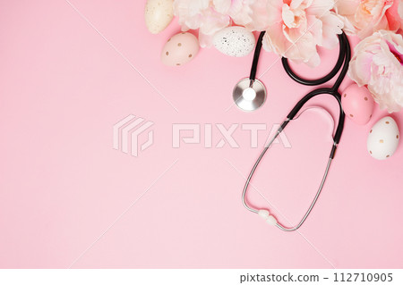 Stethoscope with Easter eggs and pink flowers on pastel background with copy space 112710905