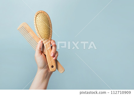 Young woman holding wooden hairbrushes on blue background Young woman holding wooden hairbrushes on blue background 112710909
