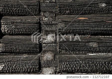 Texture (background, pattern) of a black charred log wall of a burned-out wooden house. Texture (background, pattern) of a black charred log wall of a burned-out wooden house. 112712107