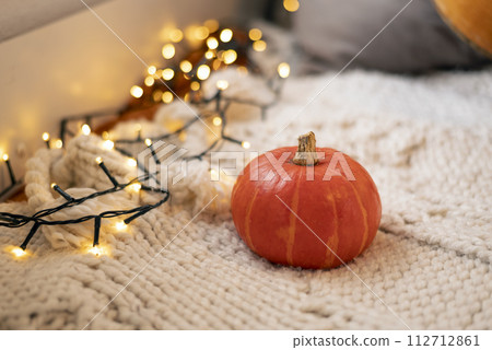Autumn still life. Pumpkin on white knitted plaid with garland - halloween home decor, concept of fall season, Warm, hygge, cozy, rustic style home decor, copy space, banner 112712861