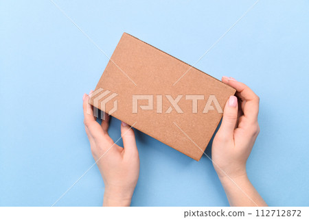 Hands holding craft paper gift box with as a present for Christmas, new year, valentine day or anniversary on blue background, top view Hands holding craft paper gift box with as a present for Christmas, new year, valentine day or anniversary on blue background, top view 112712872