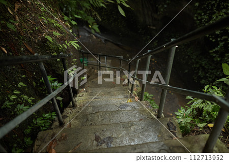 Moss-covered stairs lead to a mountain crevice with a waterfall in the jungle on the popular tourist island of Bali. Moss-covered stairs lead to a mountain crevice with a waterfall in the jungle on the popular tourist island of Bali. 112713952
