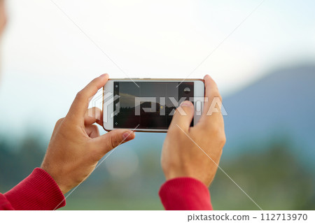 A young man stands on the side of the road near a rice paddy and takes a picture with his phone of Mount Agung on the popular tourist island of Bali. A young man stands on the side of the road near a rice paddy and takes a picture with his phone of Mount Agung on the popular tourist island of Bali. 112713970