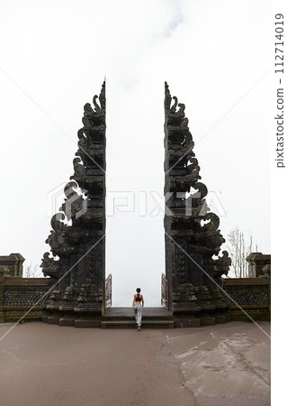 A woman stands at the Balinese traditional gate in the clouds at the sacred temple of Pura Pasar Agung Sebudi on Mount Agung. 112714019