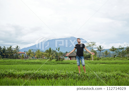 A young man poses in rice fields against the backdrop of Mount Agung volcano on the popular tourist island of Bali. 112714029