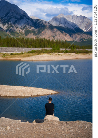 A man sits in a rocking-egg in a straw pergola enjoying the sunset 112714126