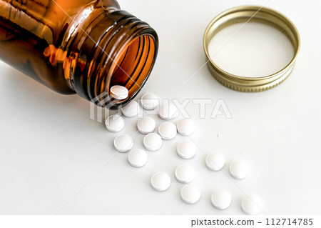 Scattered White Pills and Brown Vial, Close-Up on White Background, Concept of Pharmaceutical 112714785