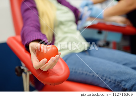 A nurse taking a blood from a young woman for examination in a modern laboratory or hospital. Young adult girl donor is at the time of donation process holding in hand a bouncy heart shape ball A nurse taking a blood from a young woman for examination in a modern laboratory or hospital. Young adult girl donor is at the time of donation process holding in hand a bouncy heart shape ball 112716309