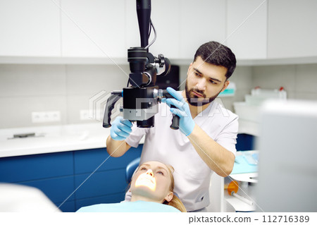 Dentist and patient at modern medical center. Doctor treats young woman teeth using microscope. Practitioner care the patient before orthodontists or prosthetics treatment. 112716389